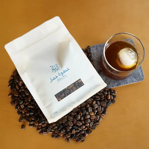 Flat-Lay von Kaffeebeutel auf gerösteten Kaffeebohnen neben Eiskaffee zur Produktpräsentation