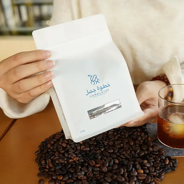Kunde hält eine weiße Kaffeetüte mit einer bedruckten Pappschachtel in einer Lifestyle-Umgebung