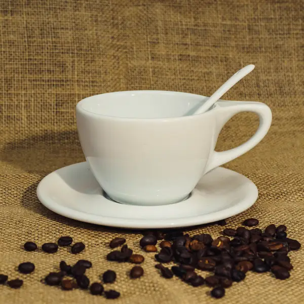 Weiße Keramik-Kaffeetasse mit flachem Deck und Henkel, die mit Kaffeebohnen ausgestellt ist