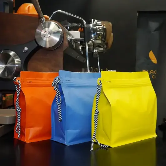 Maßgeschneiderte Kaffeebeutel mit Lanyard sind kein Nischenformat mehr in 2026. Sie sind praktisch geworden, Hochwertige Verpackungswahl für Bohnen in großen Mengen und gemahlenen Kaffee – besonders, wenn Marken sowohl Betriebskraft als auch eine saubere Füllung benötigen, Retail-tauglicher Look. At YPAK, Wir behandeln die Lanyard als mehr als nur einen Riemen. Richtig verwendet, Es wird zu einem funktionalen Fahrpunkt und zu einem visuellen Zeichen der Haltbarkeit, was beeinflussen kann, wie Käufer die Qualität in wenigen Sekunden beurteilen. Großverpackung hat eine ständige Herausforderung: Sie muss im Back-of-House hart arbeiten, Dennoch vertreten sie die Marke im Front-of-House. Das bedeutet Stabilität, Zuverlässige Wiederabschlüsse, Gasmanagement, und Bequemlichkeit. Wenn diese Elemente zusammenkommen, Die Tüte hört auf, 